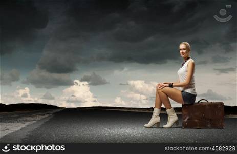 Traveling concept. Young girl traveler in shorts sitting on suitcase