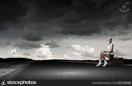 Traveling concept. Young girl traveler in shorts sitting on suitcase