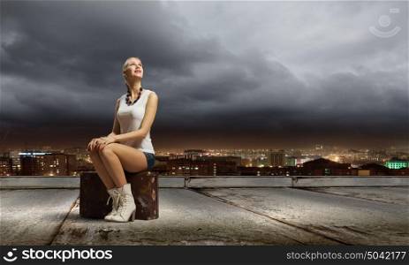 Traveling concept. Young girl traveler in shorts sitting on suitcase