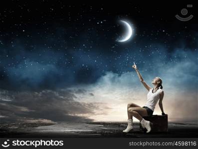 Traveling concept. Young girl traveler sitting on bag at night