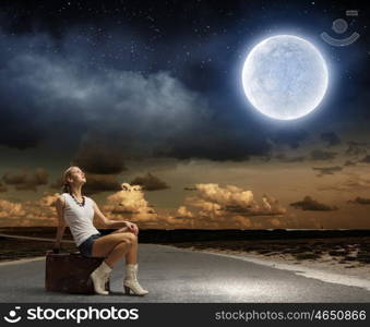 Traveling concept. Young girl traveler sitting on bag at night