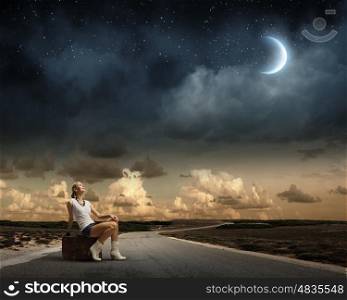 Traveling concept. Young girl traveler sitting on bag at night