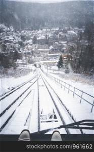 Traveling funicular railway vehicle and window view of the snowy railroad tracks, the snowy forest, and a snow-covered Bad Wildbad town, in Germany.