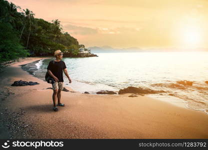 traveling man and dslr camera walking on sand beach against sunset sky