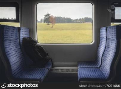 Traveling through Germany concept image with German regional train interior with blue chairs, luggage and an autumn landscape on the window.