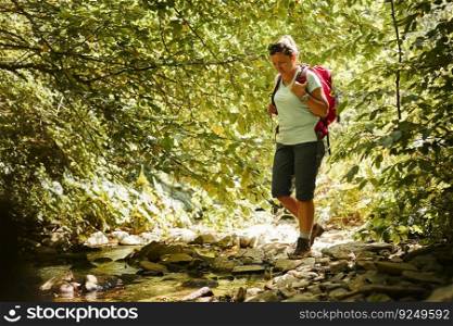 Traveling trekking with backpack concept image. Backpacker female in trekking boots crossing mountain river. Woman hiking in mountains during summer trip. Vacation trip close to nature. Natural scenery