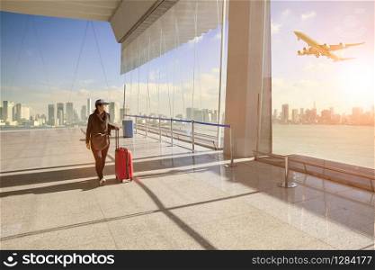 traveling woman with belonging luggage walking in airport terminal building and passenger plane flying over building in city