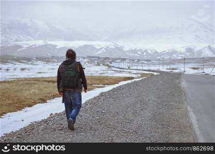 Traveller wearing backpack and walking along rural highway
