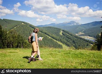 Travelling couple looking at the map over meadow and mountain view