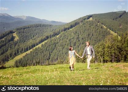 Travelling couple walking together at the summer meadow and looking around mountain view