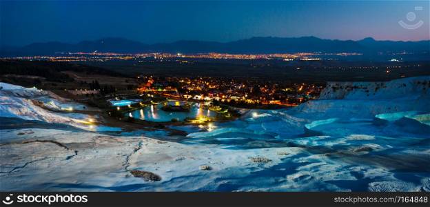 Travertine terraces and the city of Pamukkale lit by lights at night. View from above. Panorama. Denizli, Turkey. Travertine terraces and the city of Pamukkale lit by lights at night