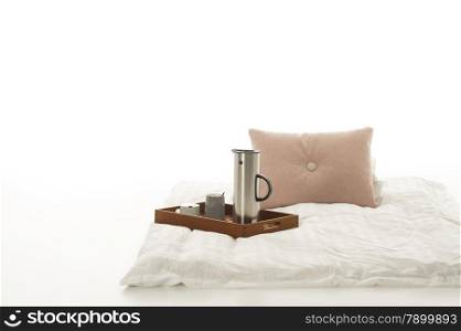 Tray with hot coffee on a soft down comforter. Tray with hot coffee on a soft plain white down comforter with beige cushion lying on a white studio background with copyspace in a minimalist interior design or decor