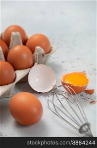 Tray with organic brown eggs with yolk,whisk and shell on light background