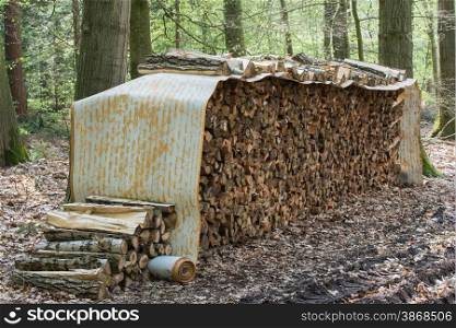 Tree logs piled up under a roll covering in a forest