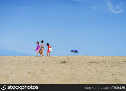 Tree young women walking on the beach sand in summer spring or autumn sunny day on the empty beach against blue sky