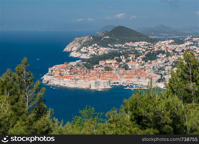 Trees frame an aerial shot of the old town of Dubrovnik and the city walls in Croatia. Fortress town of Dubrovnik in Croatia framed by trees
