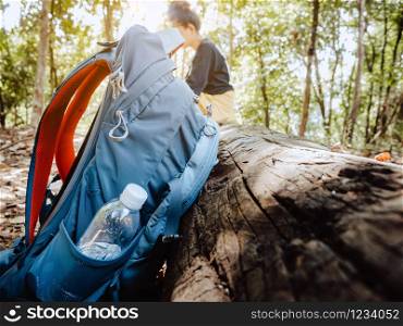 Trekking and camping adventure concept from blue backpack with tired women sitting rest on a log while walk travel nature in forest.