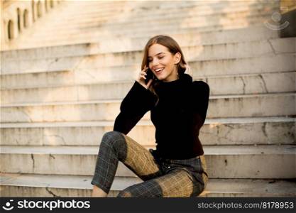 Trendu young woman with mobile phone sitting at stairs outdoor