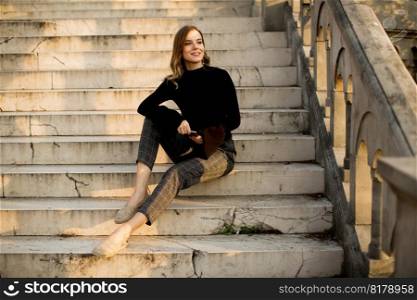 Trendu young woman with mobile phone sitting at stairs outdoor