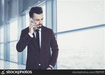Trendy and fashionable businessman walking inside the corporate building and talking on the phone (mixed)
