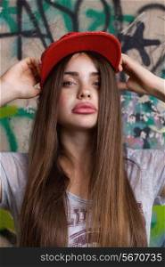 trendy beautiful long haired model posing near painted wall. red cap. grey t-shirt.