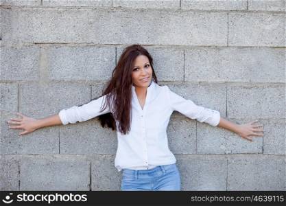 Trendy brunette woman with jeans resting on a gray wall