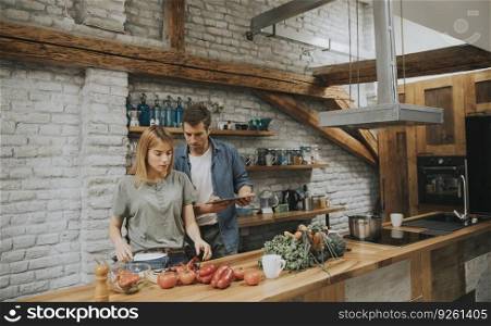 Trendy couple peeling and cutting fresh vegetables from the market in rustic kitchen