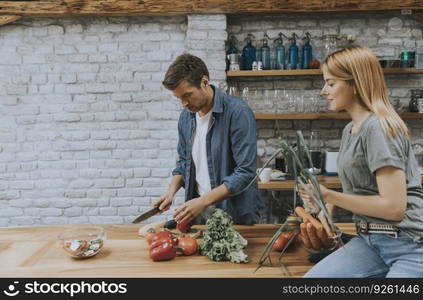 Trendy couple peeling and cutting vegetables from the market in rustic kitchen