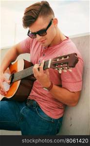 Trendy guy with guitar outdoor. Performance and show on fresh air. Young fashionable man wearing sunglasses playing classic guitar outdoor. Summer time.