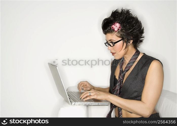 Trendy Hispanic woman typing on laptop against white background.