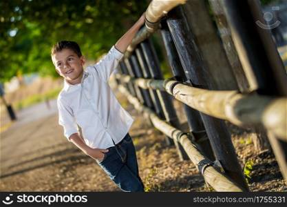 Trendy little boy walking confidently alongside fence on rural background looking away.. Stylish kid walking on nature