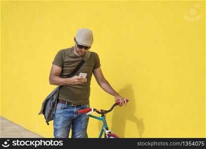 Trendy man using his smartphone outdoors while sitting on a fixed bike