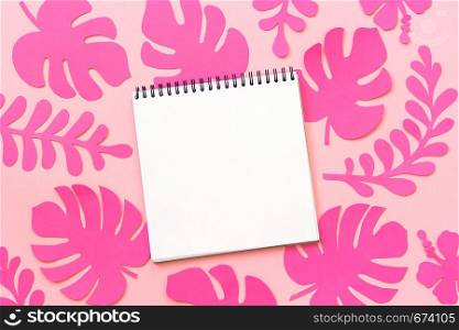 Trendy pink tropical leaves of paper and open notebook on pink background. Flat lay, top-down composition, creative paper art.. Trendy pink tropical leaves of paper and open notebook on pink background. Flat lay, top-down composition, creative paper art