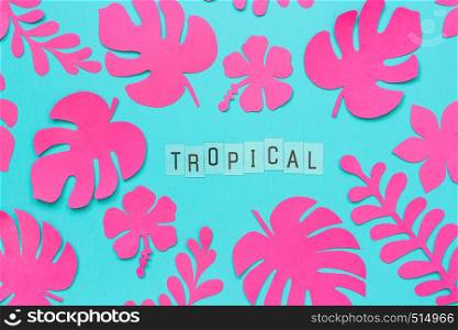 Trendy pink tropical leaves of paper and text inscription Tropical on blue background. Flat lay, top-down composition, creative paper art.. Trendy pink tropical leaves of paper and text inscription Tropical on blue background. Flat lay, top-down composition, creative paper art