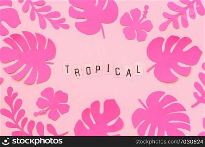 Trendy pink tropical leaves of paper and text inscription Tropical on pink background. Flat lay, top-down composition, creative paper art.. Trendy pink tropical leaves of paper and text inscription Tropical on pink background. Flat lay, top-down composition, creative paper art