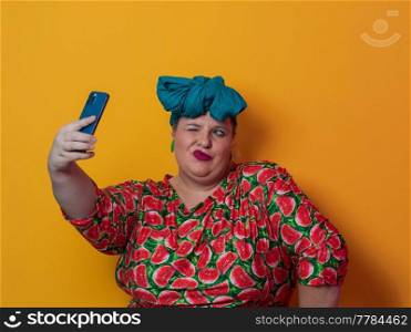 Trendy plus size woman taking selfie photo by smartphone over yellow Fortuna gold background smiling with an idea or question pointing finger with a happy face. High quality photo. Trendy plus size woman taking selfie photo by smartphone over yellow Fortuna gold background smiling with an idea or question pointing finger with a happy face.