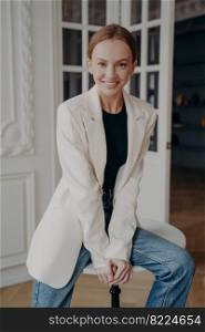Trendy stylish businesswoman. Portrait of young adult european woman in white jacket. Pretty lady is posing in apartment or studio. Concept of elegance, confidence and femininity.. Trendy stylish businesswoman. Portrait of young adult european woman in white jacket.