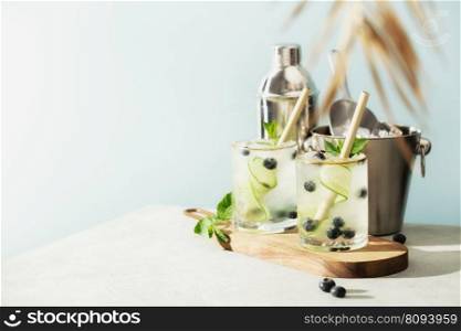 Trendy summer drinks with cucumber, mint and blueberry and Bar accessories on blue sky background