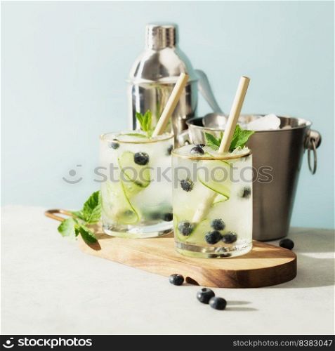 Trendy summer drinks with cucumber, mint and blueberry on blue sky background