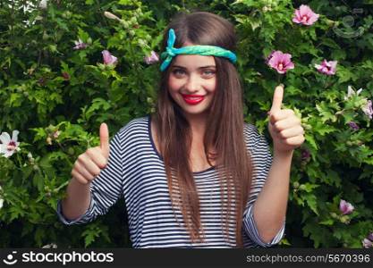 trendy teenager model with kerchief posing with flowers. Outdoor. Showing double thumb up