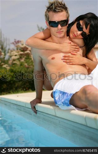 Trendy young couple laying down next to swimming pool