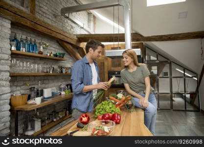 Trendy young couple peeling and cutting vegetables from the market in rustic kitchen