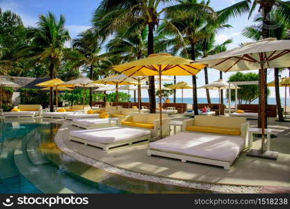 Trestle beds with beach umbrellas and palm trees by the pool. The beach and the sea are visible in the distance