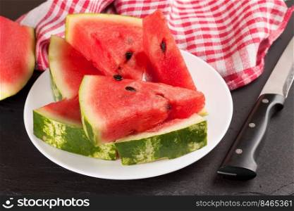 Triangle slices of watermelon on the plate on black slate background.. Sliced watermelon on the plate on blue wooden background