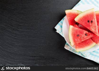 Triangle slices of watermelon on the plate on black slate background. Top view, flat lay, mockup with copy space for text. Sliced watermelon on the plate on black slate background