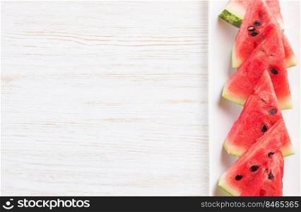 Triangle slices of watermelon on the plate on white wooden background. Top view, flat lay, mockup with copy space for text. Sliced watermelon on the plate on white wooden background