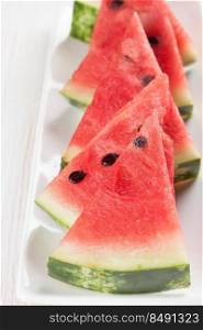 Triangle slices of watermelon on the plate on white wooden background. Vertical photo. Sliced watermelon on the plate on white wooden background