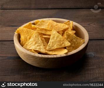 triangular nachos with spices in a round wooden bowl. brown table