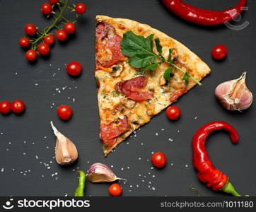 triangular piece of baked pizza with mushrooms, smoked sausages, tomatoes and cheese, black background, flat lay