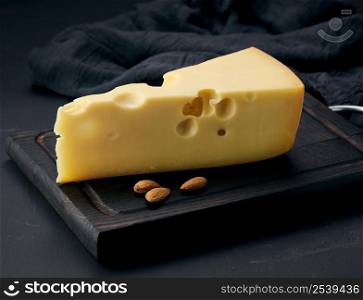 triangular piece of maasdam cheese on a brown wooden board